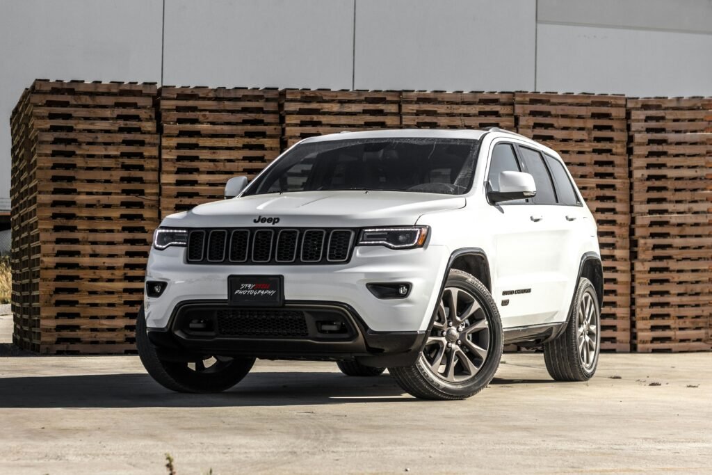 A sleek white Jeep Grand Cherokee parked in front of stacked wooden pallets, showcasing its luxury features.