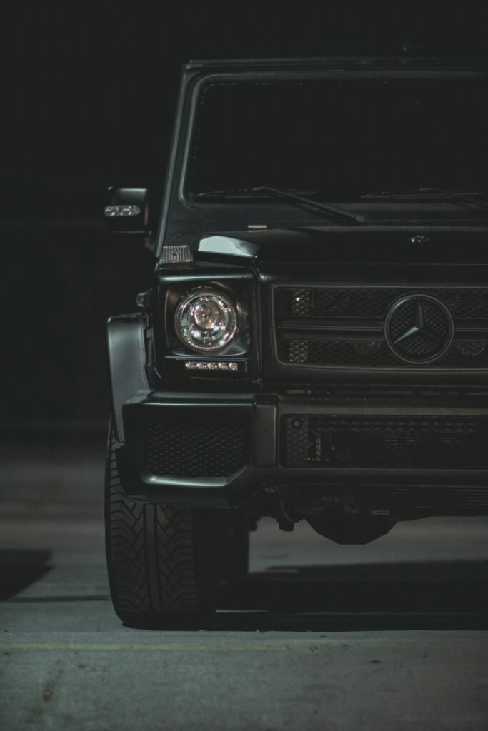 Close-up of a luxury black car's front, featuring a sleek design and emblem under nighttime lighting.